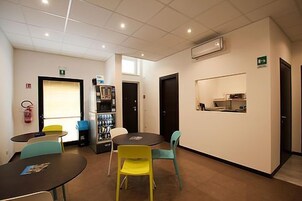 Una habitación con una mesa redonda, sillas, una máquina expendedora y una pequeña kitchenette.