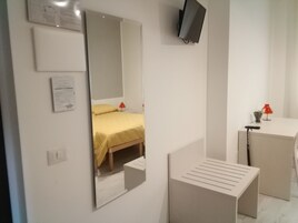 Una habitación de hotel con una cama, televisión montada en la pared, escritorio y espejo.