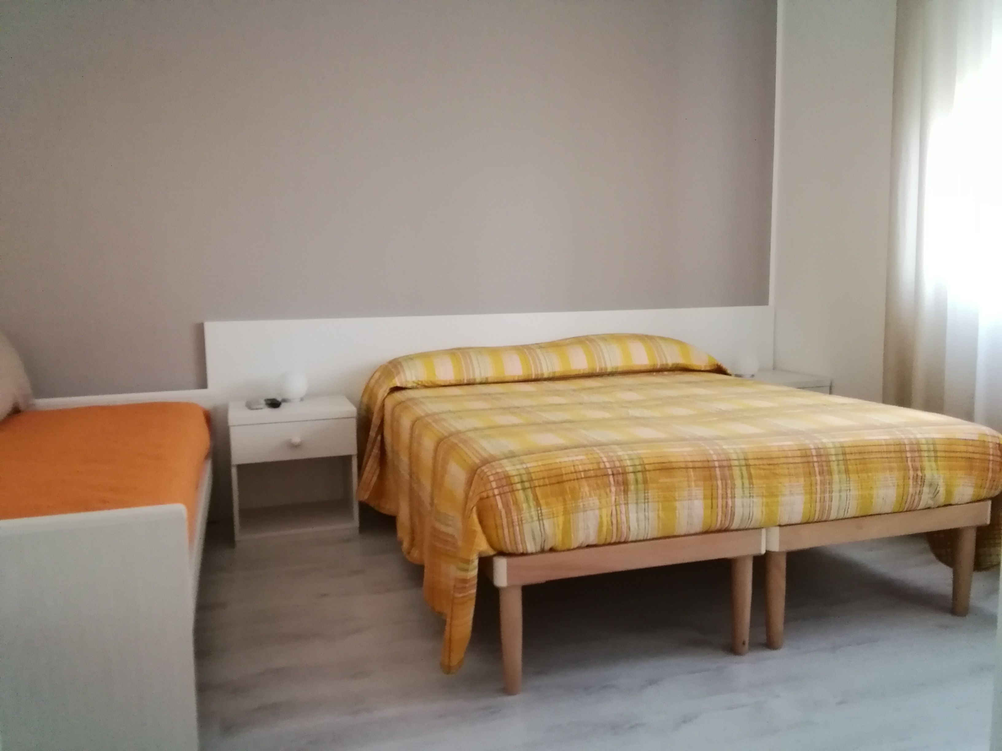 A bedroom with a bed, a nightstand, a chair, and a window with curtains.