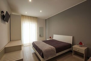 Un dormitorio moderno con una cama, mesitas de noche, un televisor y un ventanal con cortinas.