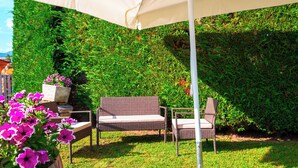 Une terrasse de jardin avec un parasol blanc, des meubles en osier et un mur végétal.