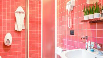 A bathroom with red tiles, a white sink, a hairdryer, a towel rack, and a potted plant.