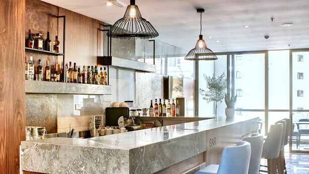 A modern bar area with a marble countertop, bar stools, and a variety of bottles. - The District Hotel (St. Julian's)