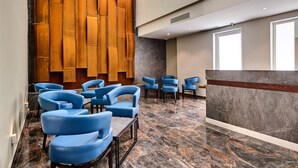 A modern lobby with blue chairs, a reception desk, and a wooden wall. - The District Hotel (St. Julian's)