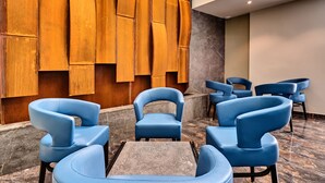 A lobby with blue upholstered chairs arranged around a central table, a wooden wall with vertical panels, and a marble floor. - The District Hotel (St. Julian's)