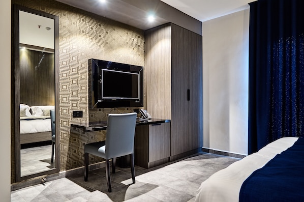A modern hotel room with a bed, a desk with a chair, a television, and a wardrobe.
