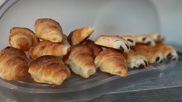 Muovinen rasia, joka on täynnä erilaisia leivonnaisia, kuten croissantteja ja suklaatäytteisiä leivonnaisia.