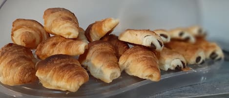 Um recipiente de plástico cheio de diversos doces, incluindo croissants e pastéis de chocolate.