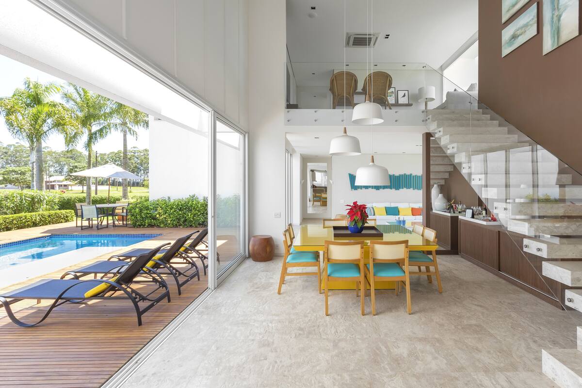 A modern interior with a dining area, a staircase, and a poolside area with lounge chairs.