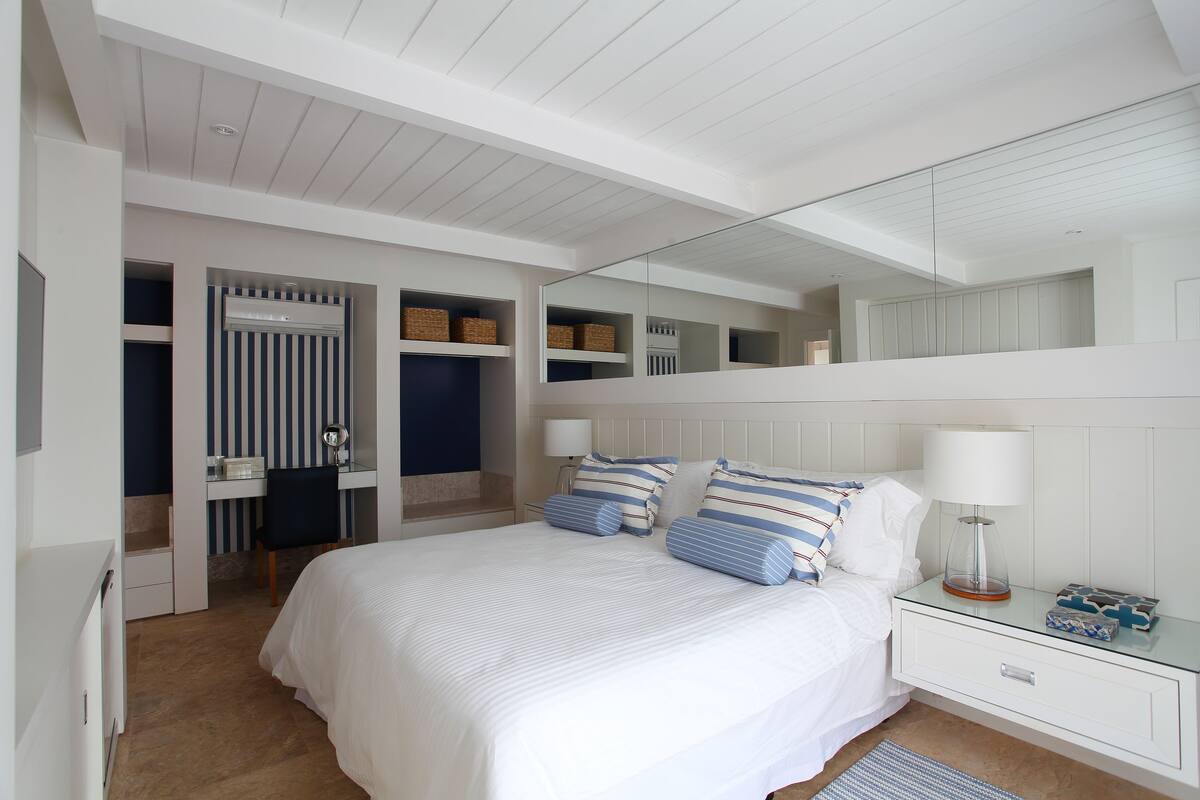 A bedroom with a large bed, a bedside table, a nightstand, a mirror, and built-in shelving.