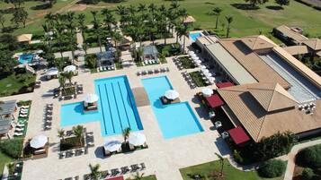 An aerial view of a resort with multiple swimming pools, sun loungers, and palm trees.