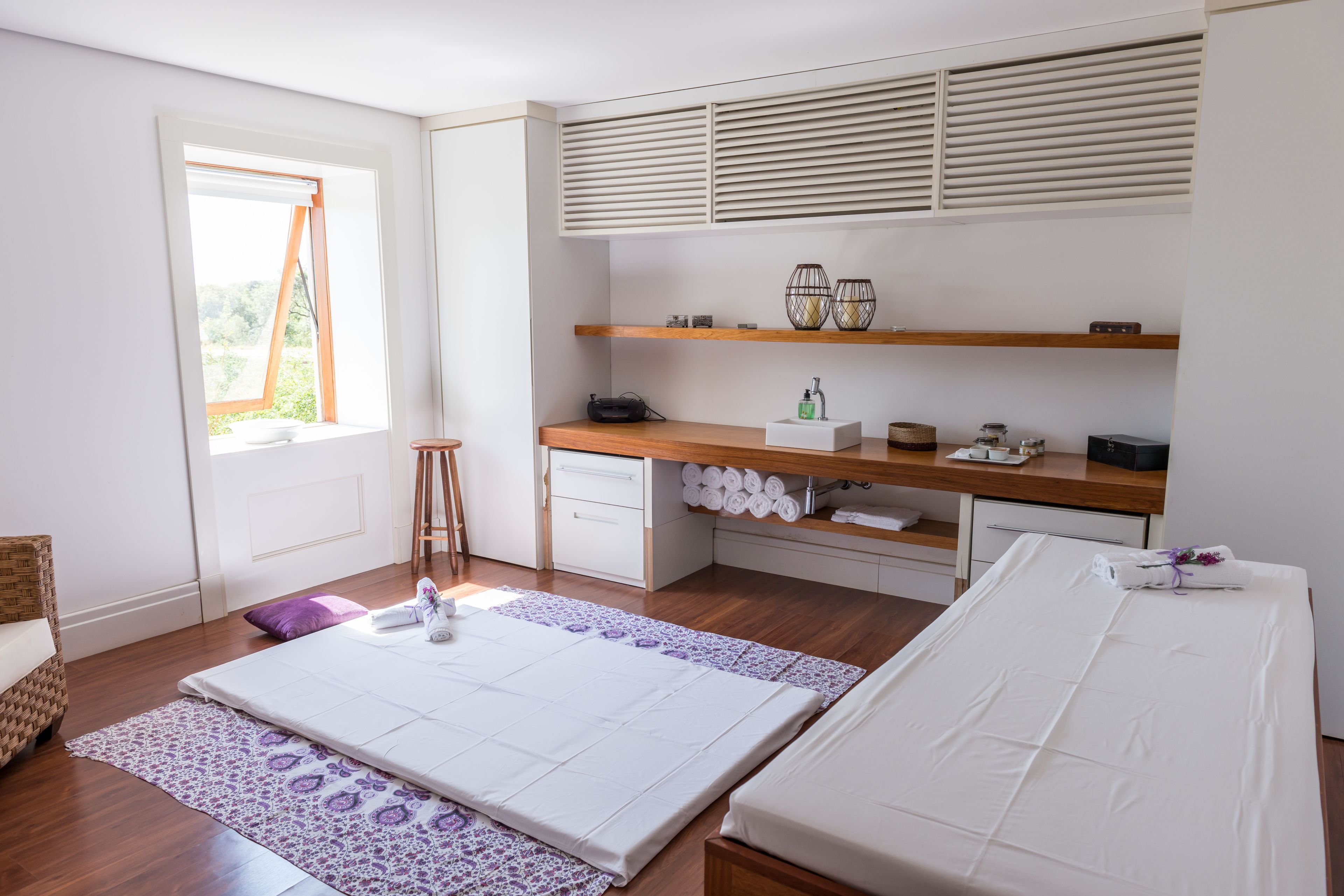 Een slaapkamer met een bed, een bureau, planken, een raam en een badkamergedeelte.