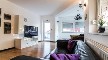 A modern living room with a leather sofa, a flat-screen TV, a white cabinet, and a potted plant.
