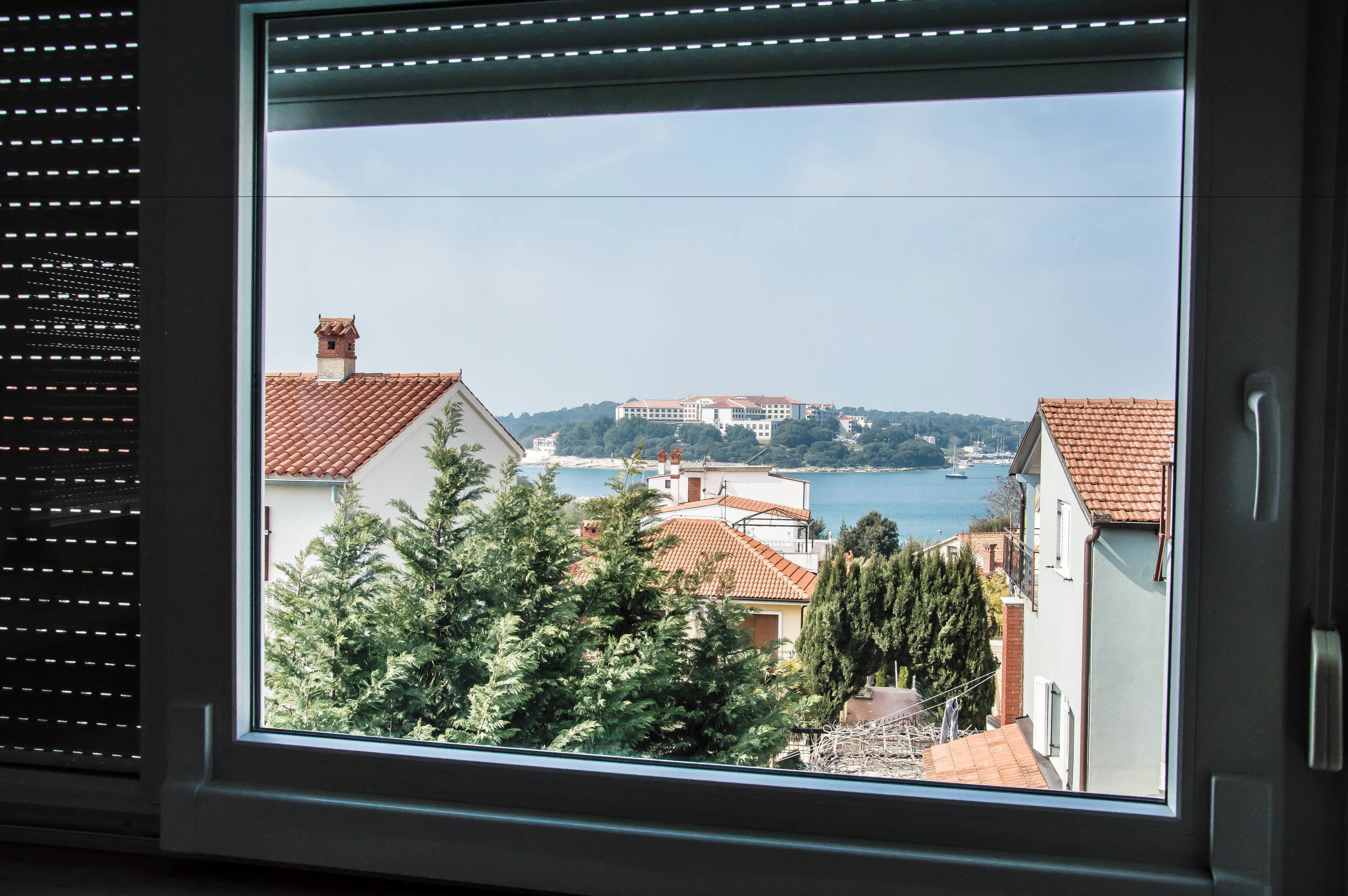Blick aus einem Fenster auf eine Küstenstadt mit Gebäuden, Bäumen und einem Wasserabschnitt.