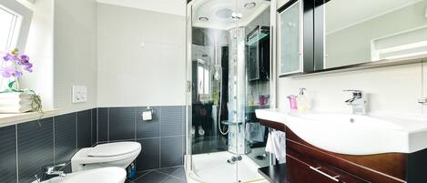 Un baño moderno con ducha de vidrio, dos inodoros y un tocador con espejo.