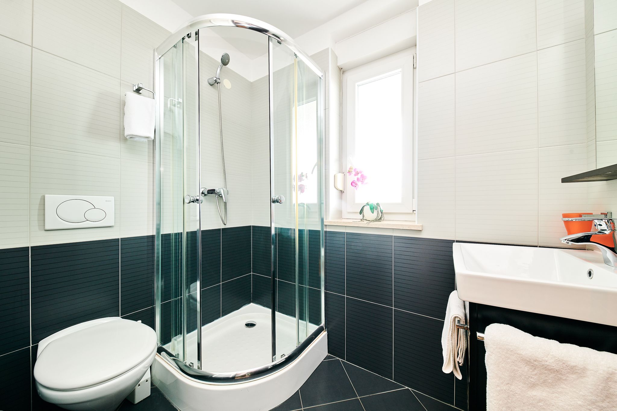 A modern bathroom with a glass-enclosed shower, a white toilet, and a sink with a mirror.