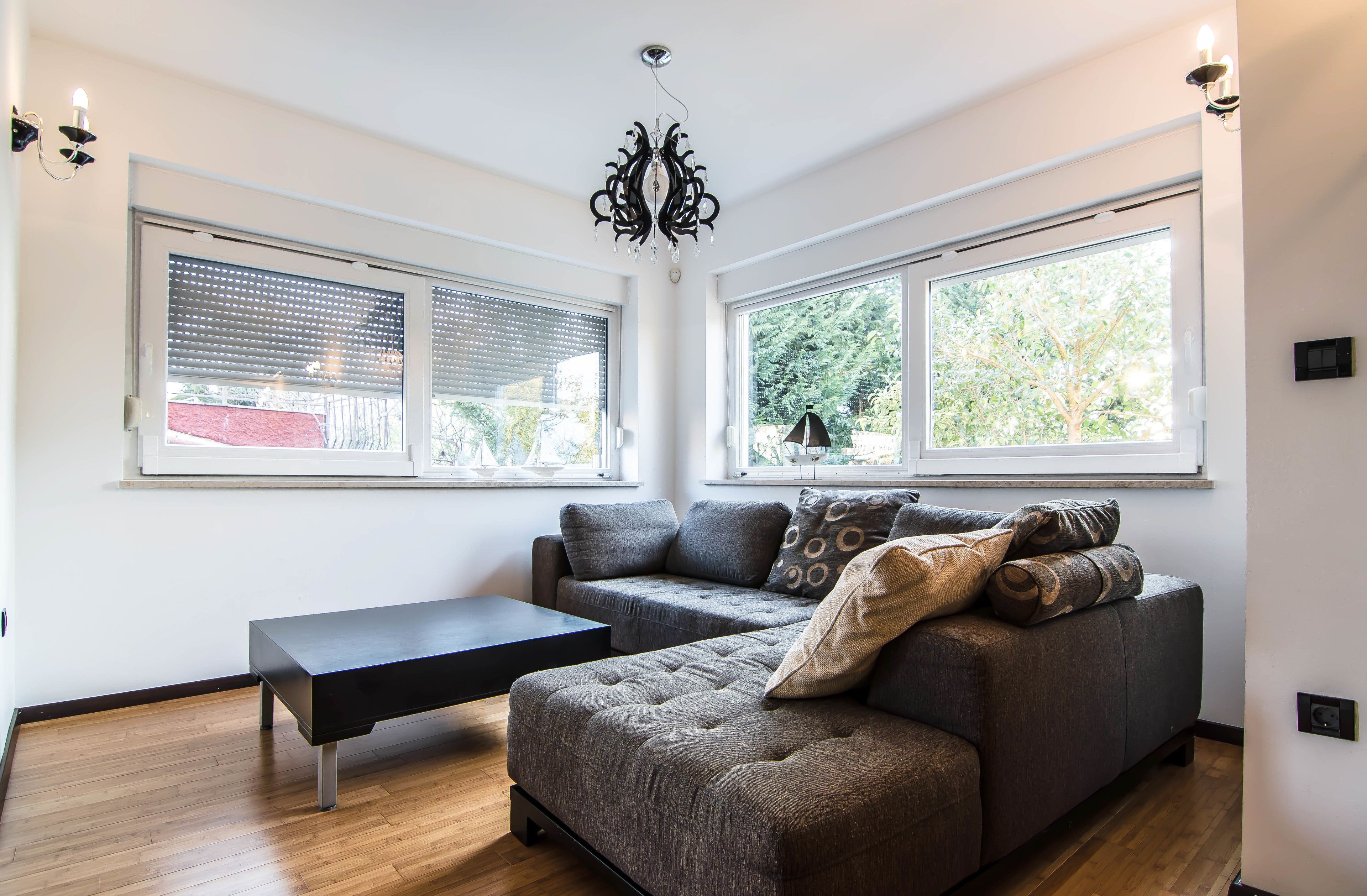 Una sala de estar moderna con un sofá modular, una mesa de centro negra y dos ventanas con persianas.