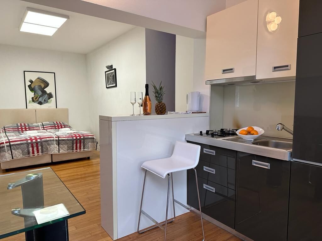 Une cuisine compacte avec un coin bar, un tabouret de bar blanc et un lit recouvert d’une couvre-lit à motifs.