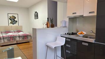 A compact kitchen with a bar area, a white bar stool, and a bed with a patterned bedspread.
