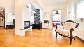 Un salon spacieux avec une cheminée, un canapé noir, un fauteuil blanc et un grand miroir.