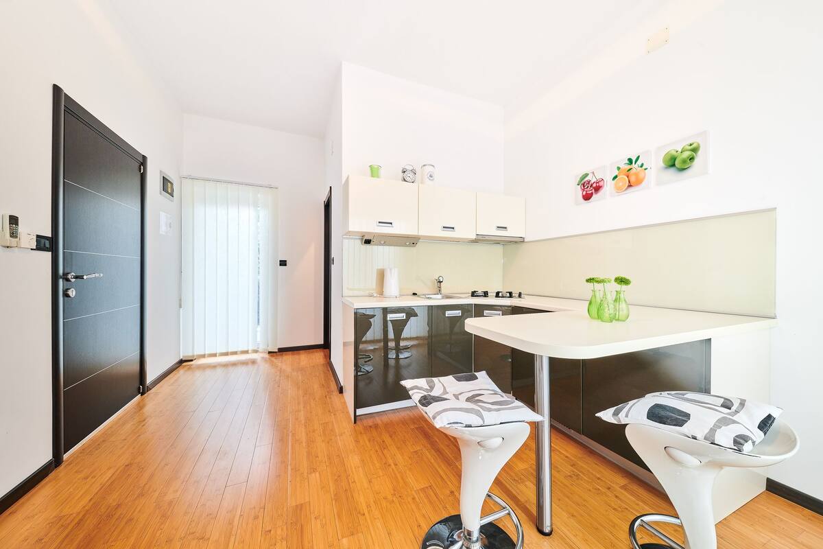 A modern kitchen with a white countertop, two bar stools, and a dining table.