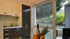 Une cuisine moderne avec des meubles de couleur sombre, une table à manger avec un plateau en verre et un saladier rempli de fruits.