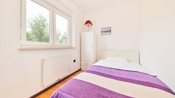 Un dormitorio con cama, ventana, radiador, armario y lámpara.
