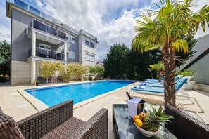 A modern building with a swimming pool, lounge chairs, and a dining table with fruits. - Stella Adria (Medulin)