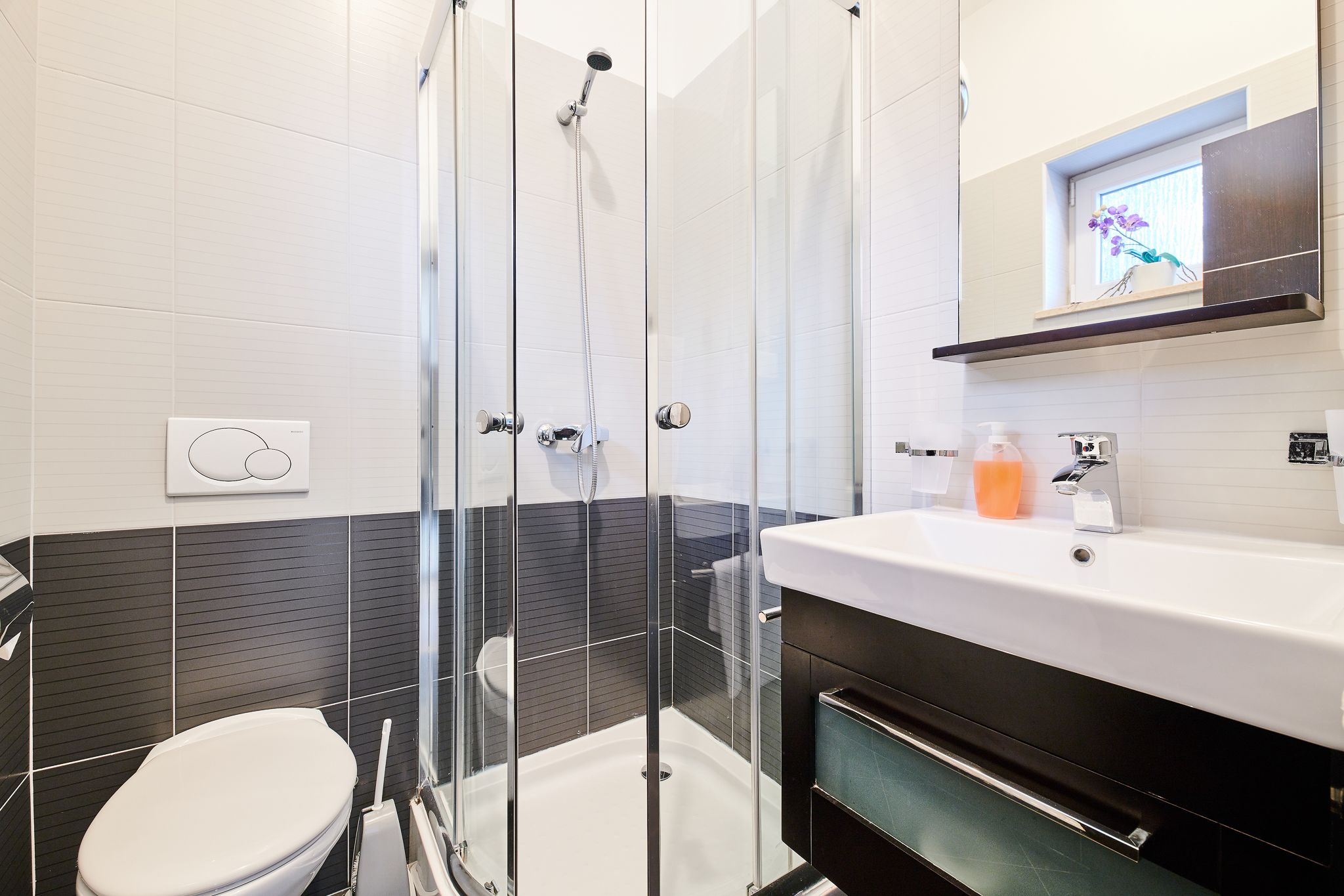 A modern bathroom with a glass-enclosed shower, a white toilet, and a black and white tiled wall.