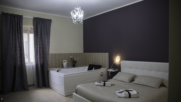 A modern bedroom with a large bed, a built-in bathtub, and a chandelier. - Il Centro Short Lets (Valguarnera Caropepe)