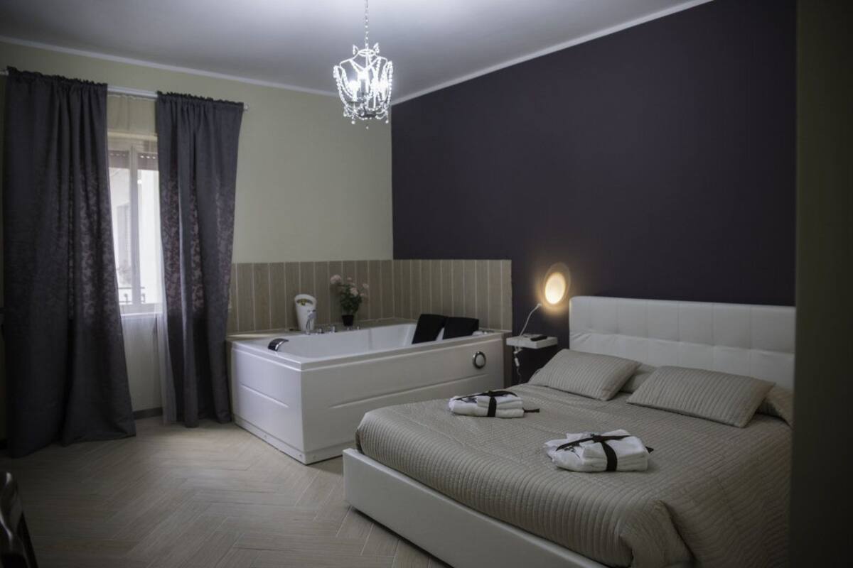 A modern bedroom with a large bed, a built-in bathtub, and a chandelier.
