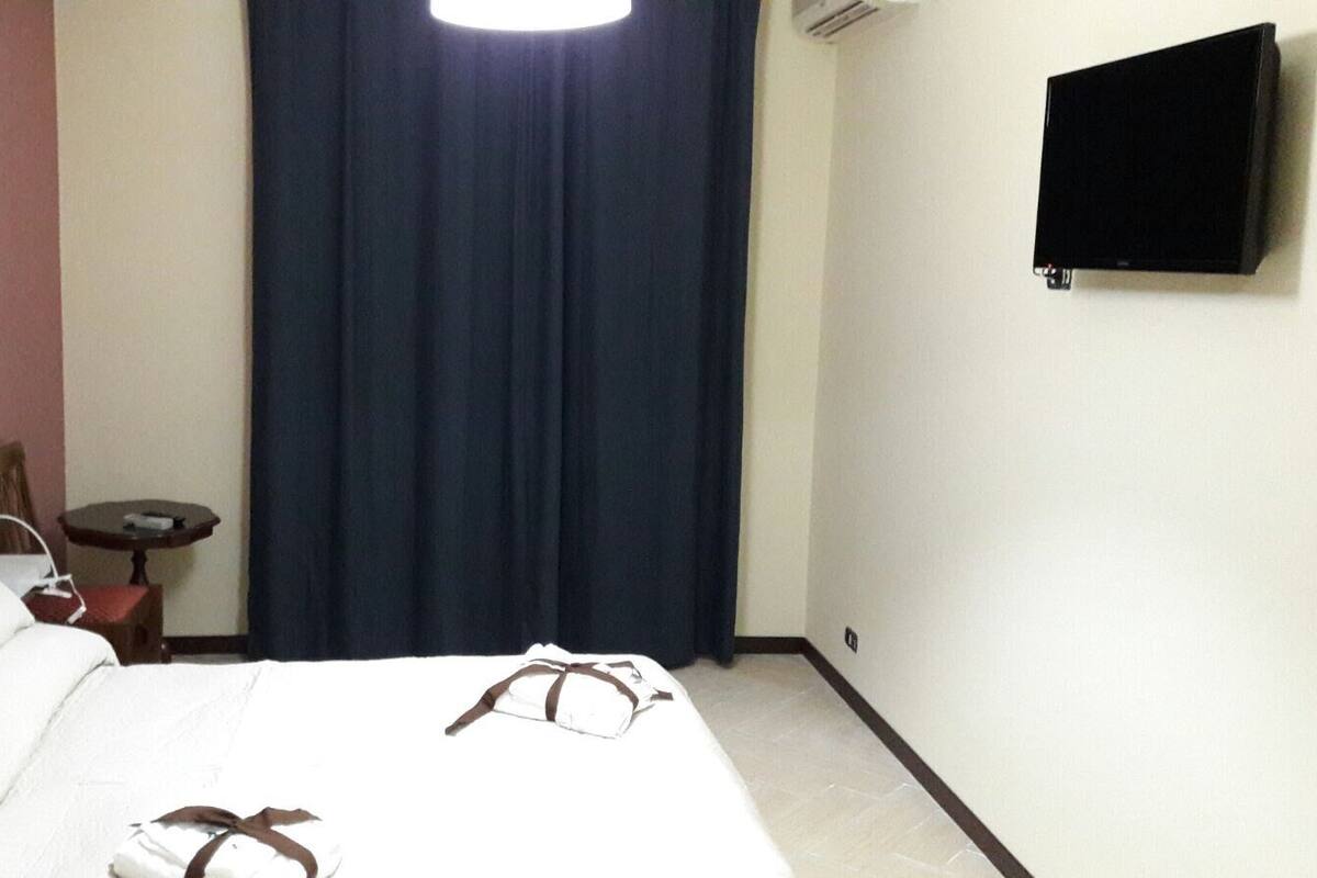 A hotel room with a bed, a small table, a chair, a TV, and a curtain.