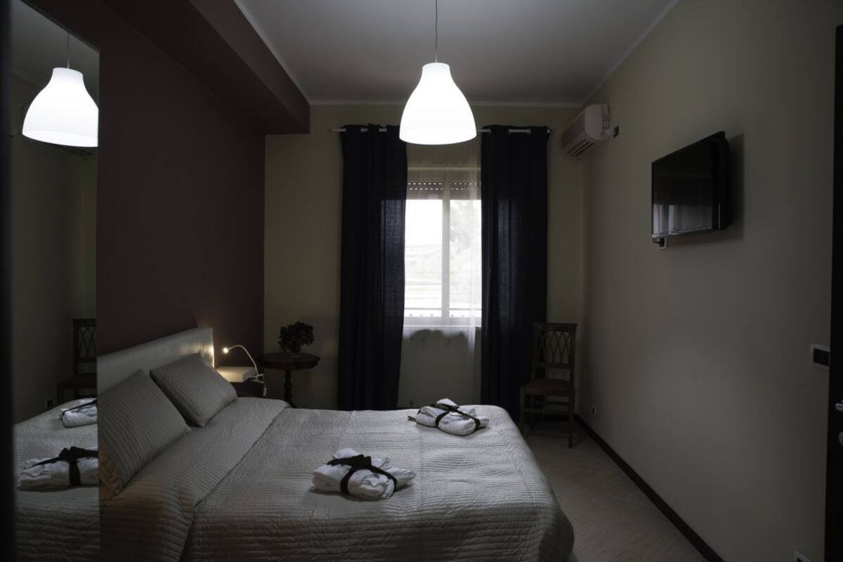A hotel room with a bed, two pendant lights, a TV, and a window with curtains.