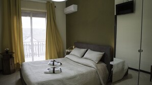 A hotel room with a large bed, a nightstand, a TV mounted on the wall, and a window with curtains. - Il Centro Short Lets (Valguarnera Caropepe)