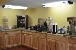 Una cocina con armarios de madera, microondas, cafetera y varios electrodomésticos.