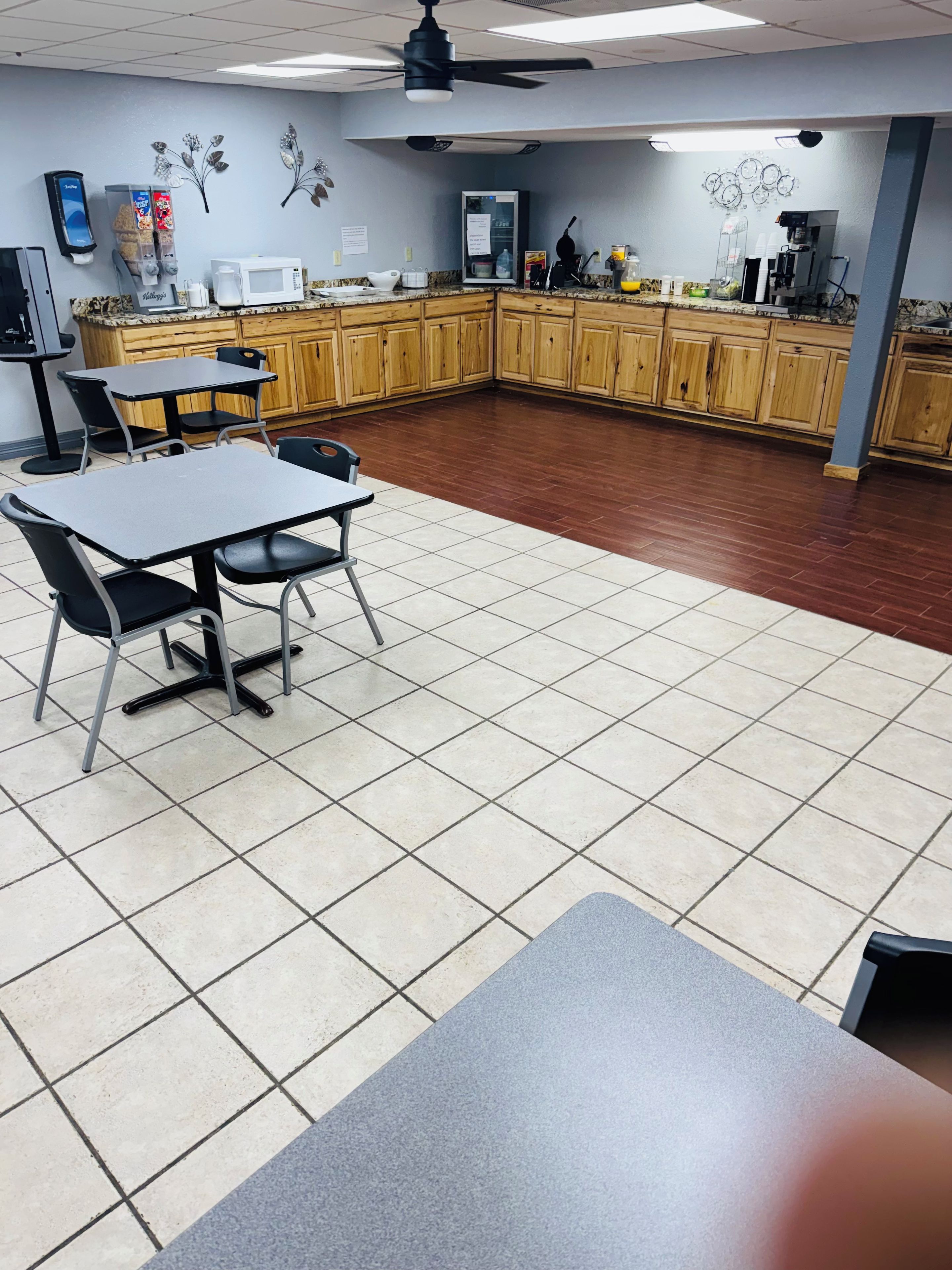 A clean, well-lit room with a tiled floor, a table with chairs, a microwave, and a refrigerator.