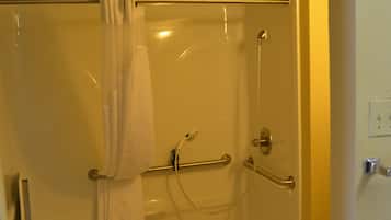 Ducha a nivel con barra de apoyo, inodoro blanco y una toalla colgada en la puerta.