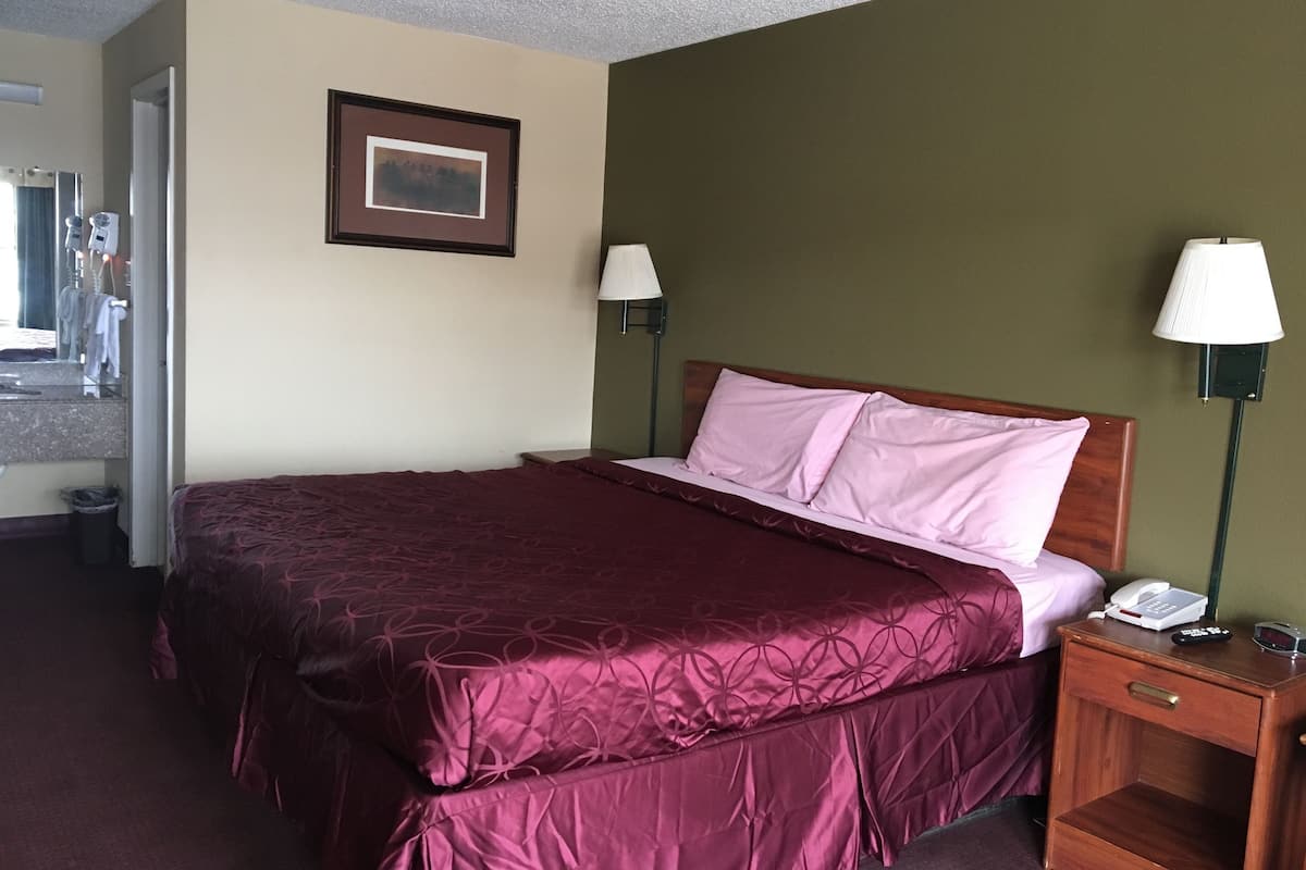 Quarto de hotel com uma cama grande, uma mesa de cabeceira com telefone e um quadro na parede.