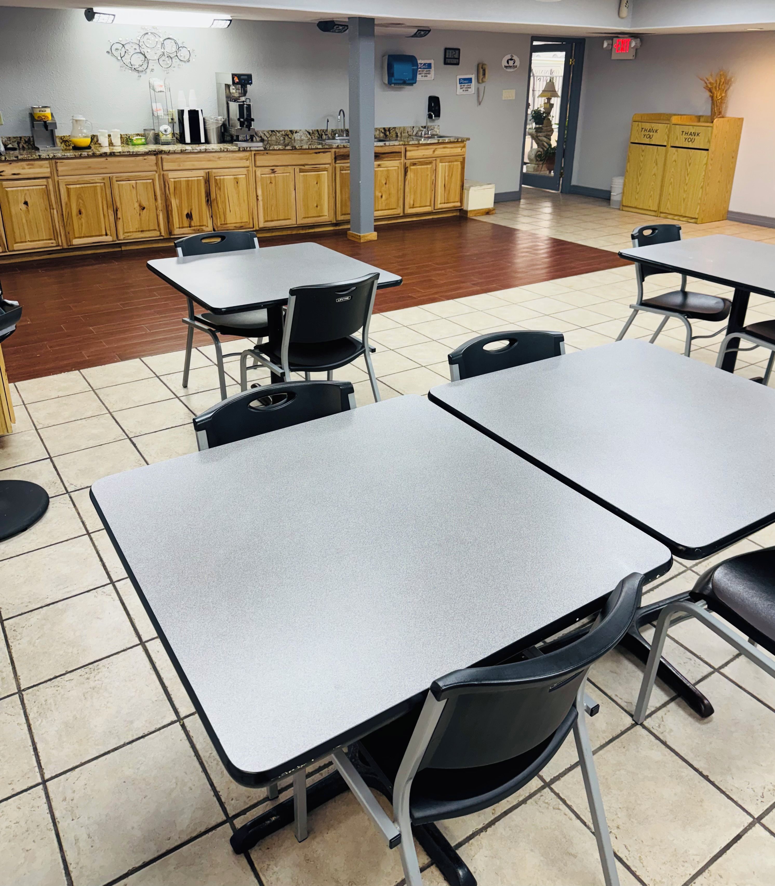 A clean, well-lit room with tables and chairs, a kitchen area in the background, and a door leading outside.