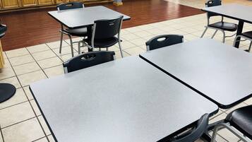 A clean, well-lit room with tables and chairs, a kitchen area in the background, and a door leading outside.