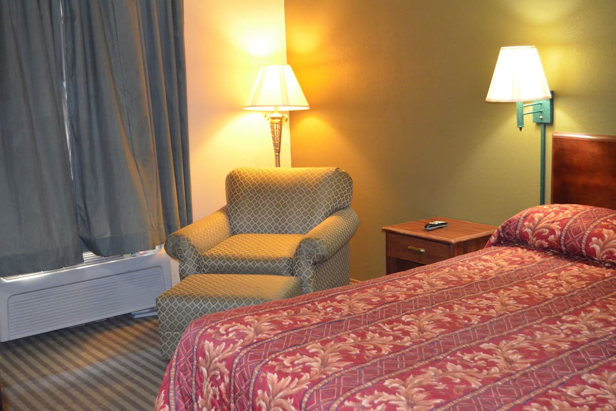 Quarto de hotel com cama, poltrona, mesa de cabeceira, abajur e aquecedor.