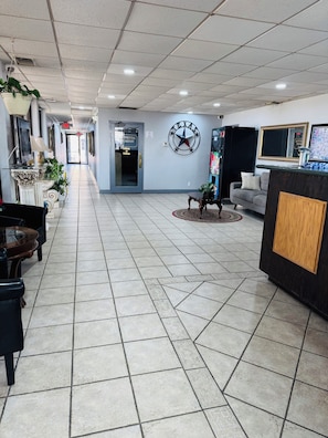 A hotel lobby with a reception desk, a clock, a coffee machine, and a sofa.