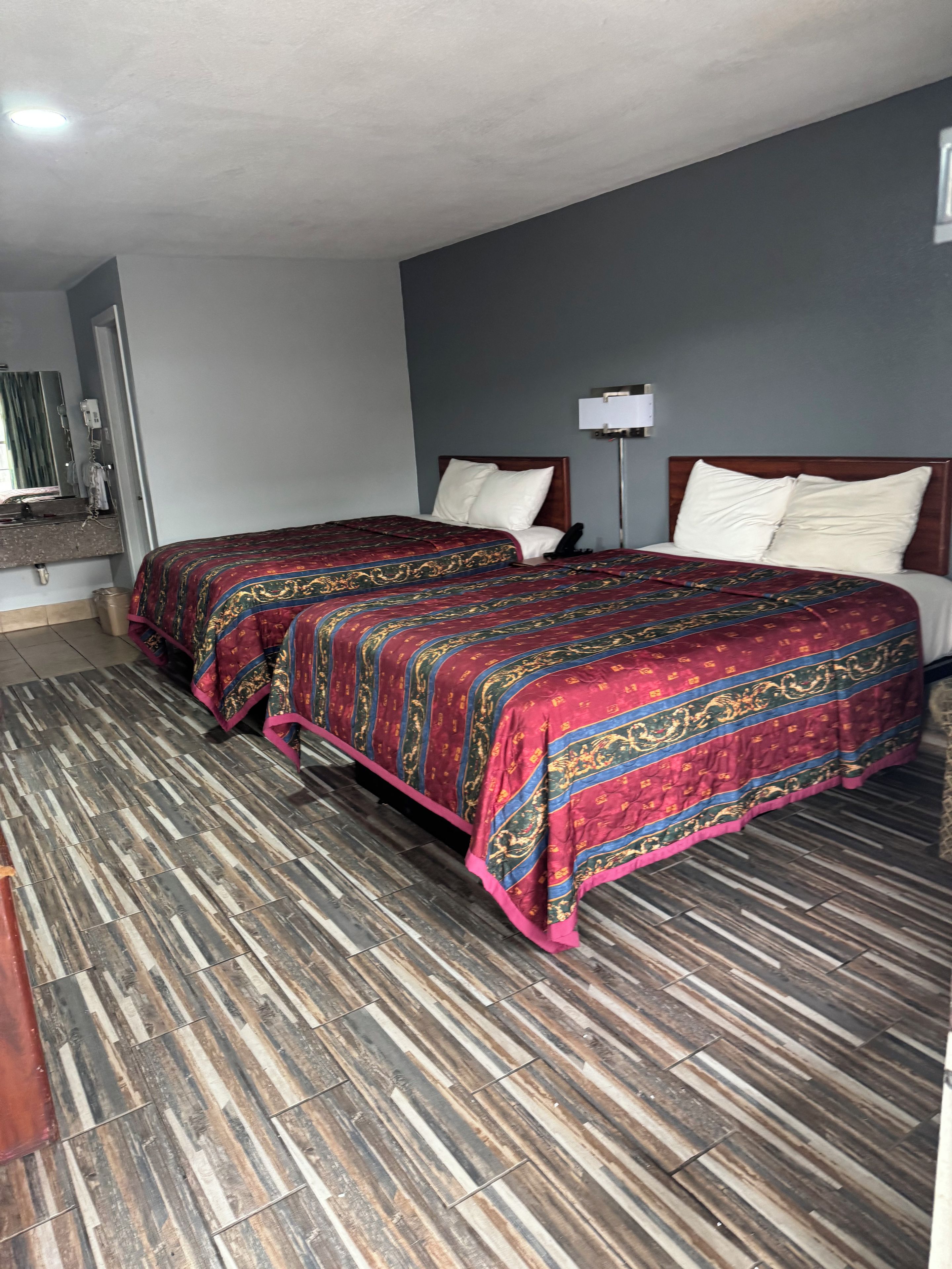 A hotel room with two beds, a wooden floor, and a grey wall.