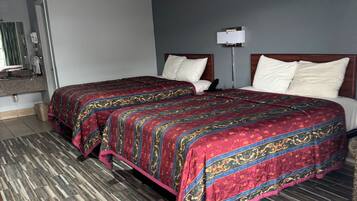 A hotel room with two beds, a wooden floor, and a grey wall.