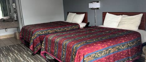 A hotel room with two beds, a wooden floor, and a grey wall.