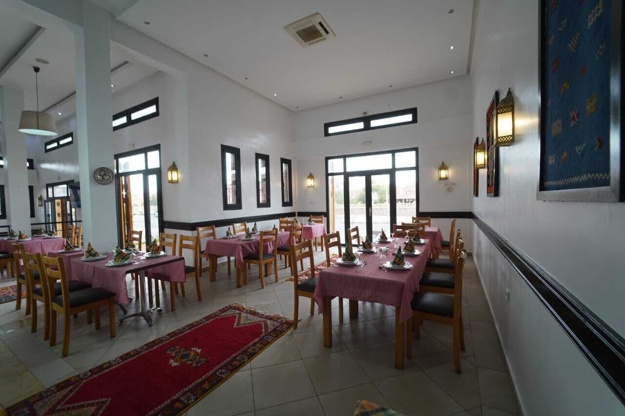 Un comedor con mesas dispuestas para comer, ventanas amplias y luces fijadas a la pared.