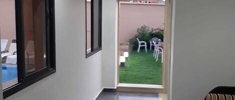A hotel corridor with a red carpet, a window, and a door leading to a patio area.