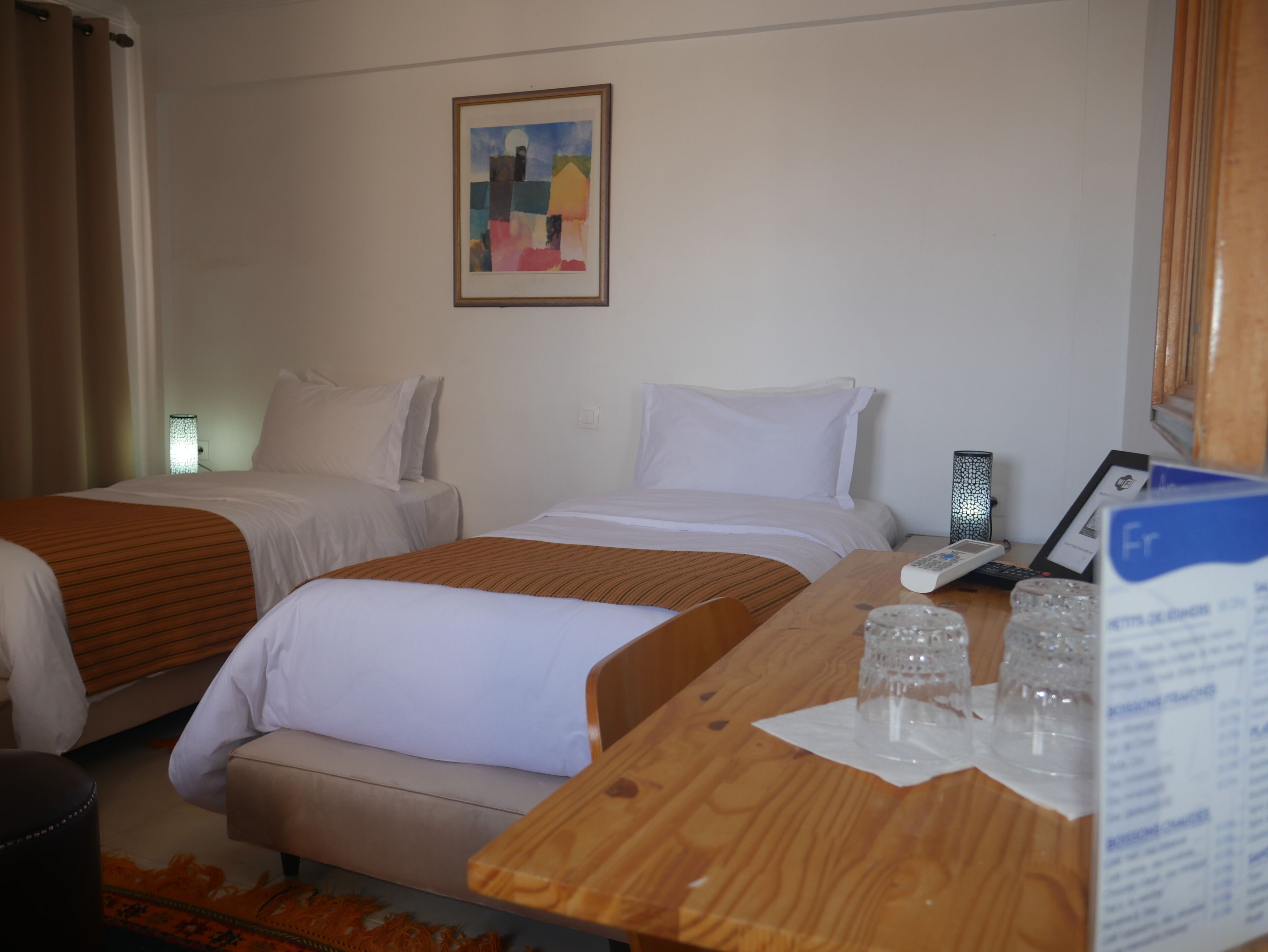 Habitación de hotel con dos camas, un escritorio de madera, una lámpara y un cuadro en la pared.