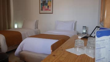 Habitación de hotel con dos camas, un escritorio de madera, una lámpara y un cuadro en la pared.