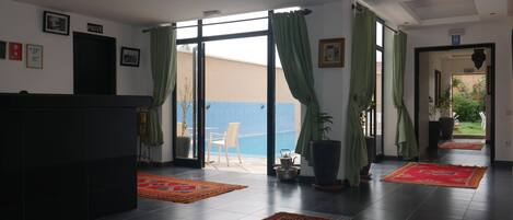 A hotel lobby with a reception desk, a seating area with a view of the sea, and a hallway leading to another room.